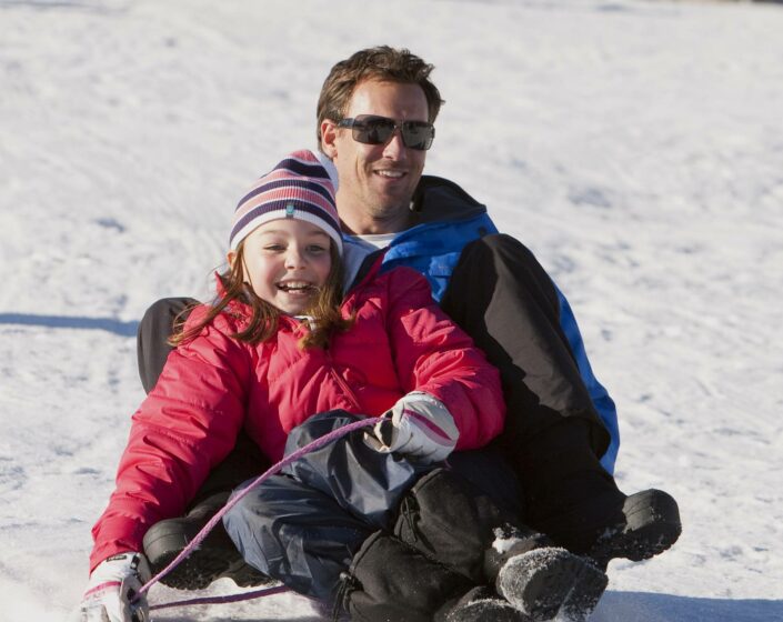 A girl tobogganing with their father in The Lake Mountain Alpine Resort