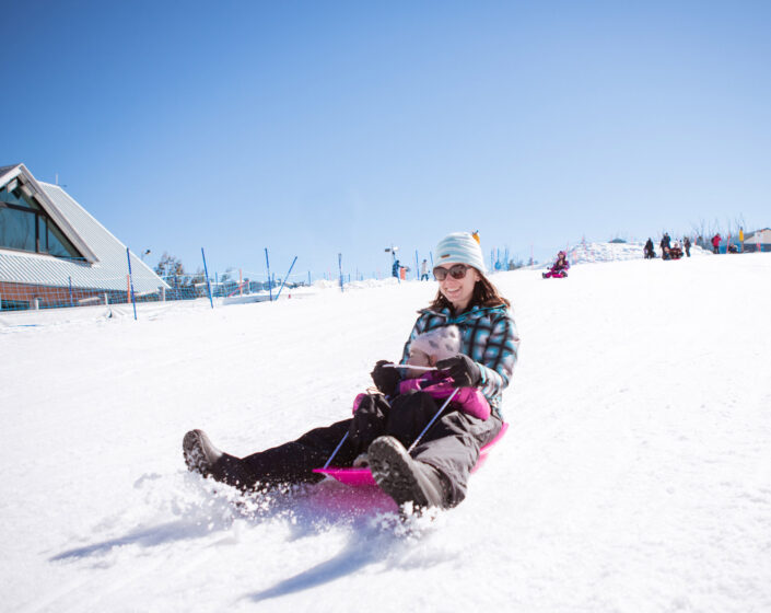 A toddler tobogganing with an adult in The Lake Mountain Alpine Resort