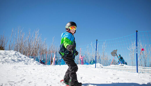 a kid standing up on a snowboard facing down the hill