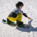turning-on-a-snowboard a kid crouching down on the ground ready to turn on their snowboard